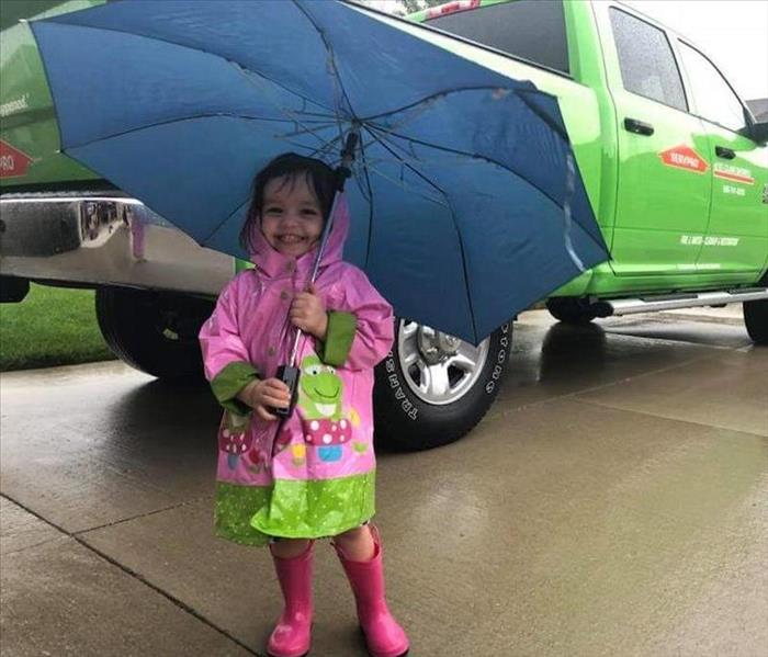 little girl under umbrella by SERVPRO truck in driveway