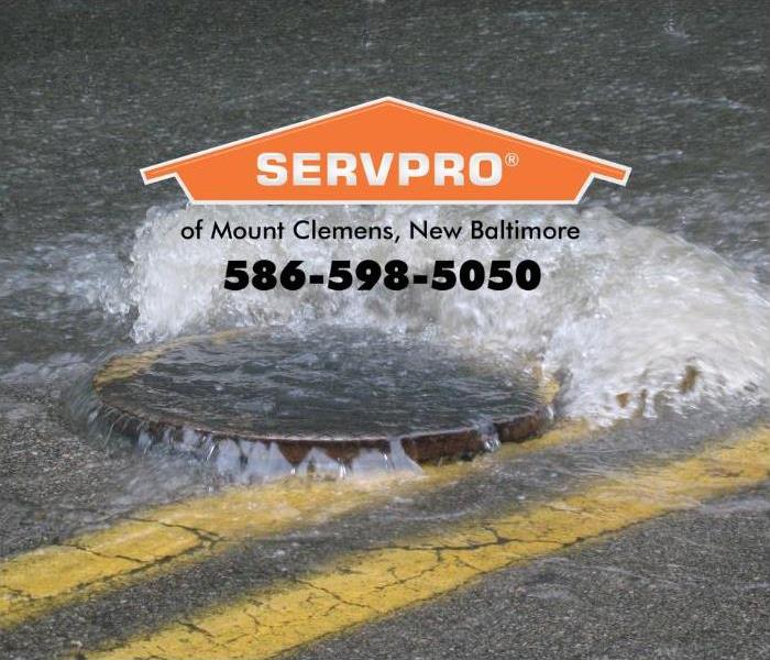 A flooded street is shown with water coming up from below a drain cover. 