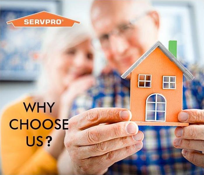 Old Couple holding a little SERVPRO house smiling 