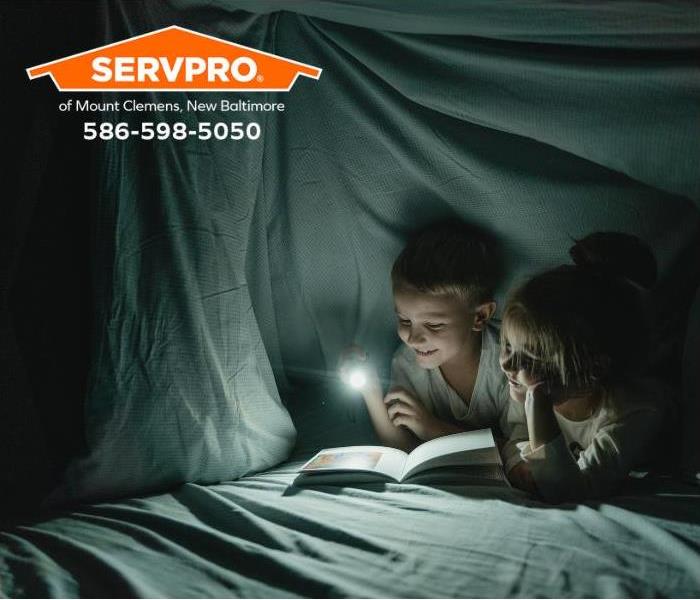 Children read a book using a flashlight during a power outage.